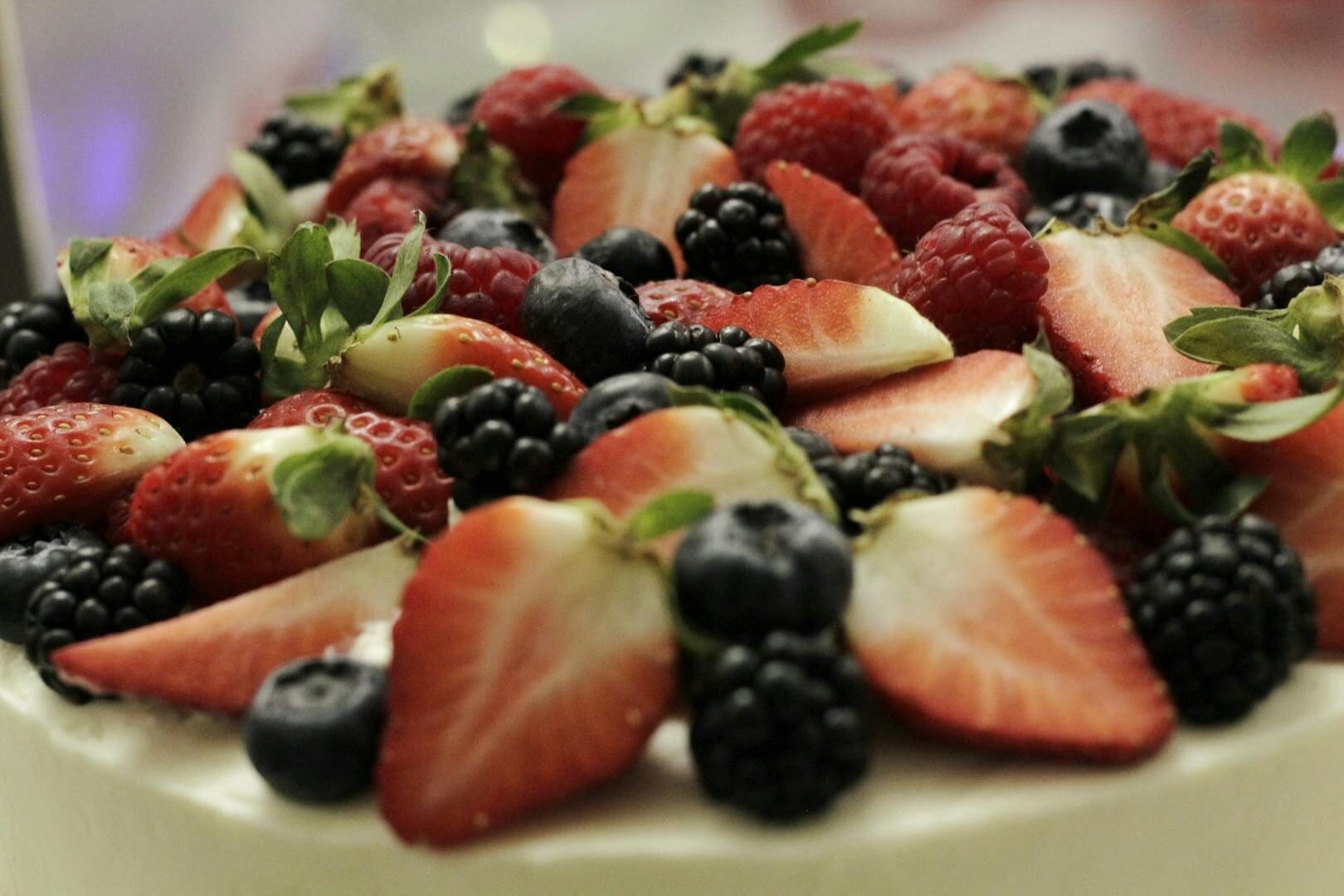 A vibrant close-up of a dessert topped with fresh strawberries, raspberries, blueberries, and blackberries.