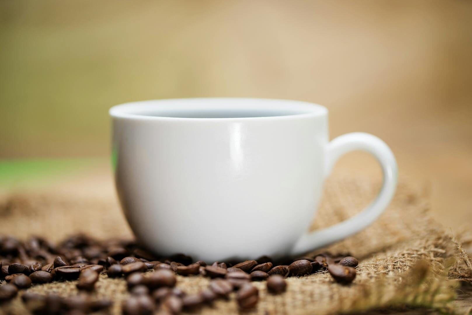 White coffee cup resting on burlap with scattered coffee beans in warm lighting.