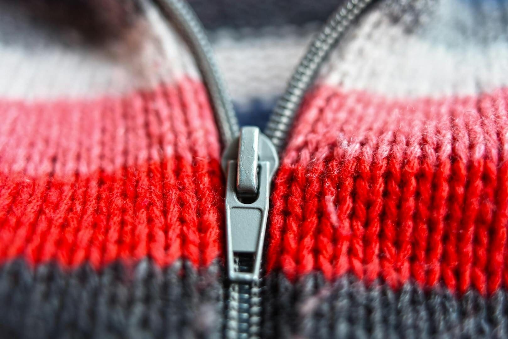 A detailed view of a metal zipper on a red and blue striped knitted garment.