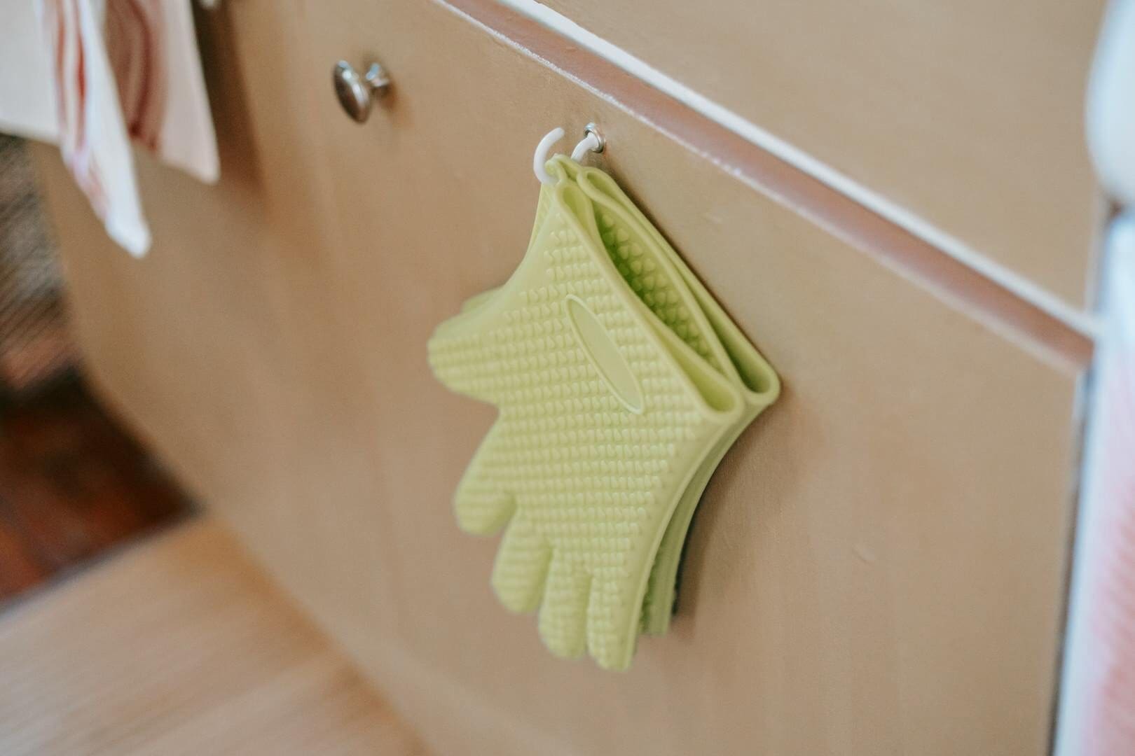 From above of pair of potholders made of silicone with bumpy surface hanging on hook at home
