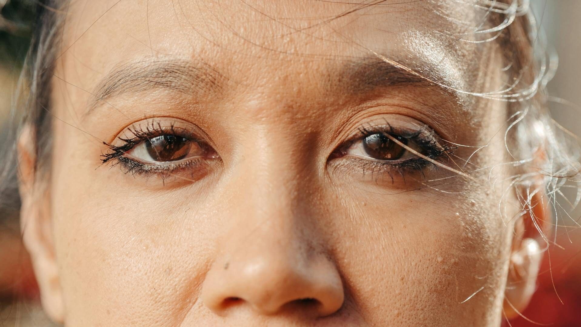 Extreme close-up of a woman's eyes with soft natural lighting, showcasing eye makeup and skin texture.