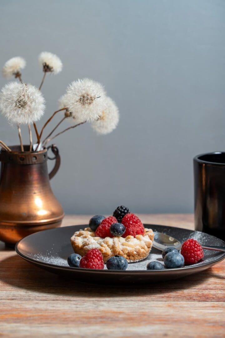 berry tarts, berry, raspberries, blueberries, blackberries, powdered sugar, black plate, coffee pot, black cup, teapot, spoon, wooden table, breakfast, dessert, pastries, vintage, still life, dried flowers, dandelions, copper vase, rustic, comfortable, food photography, close up, cute