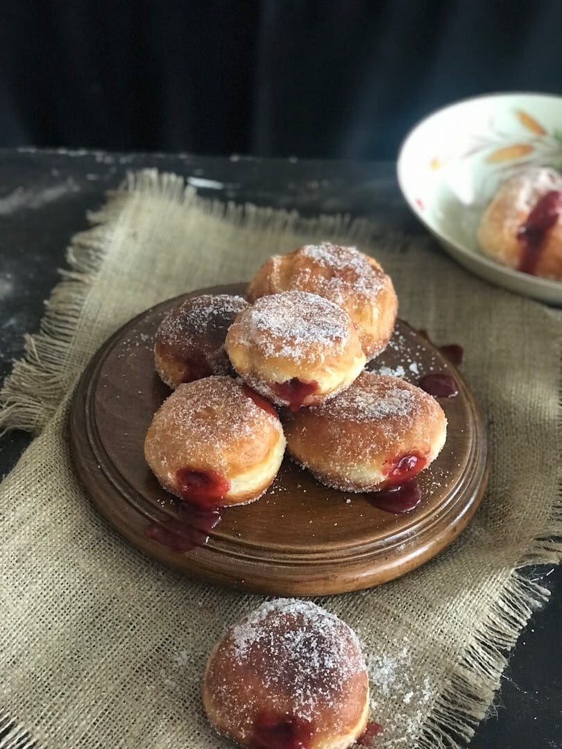 A stack of delightful jam-filled donuts sprinkled with powdered sugar on a wooden tray.