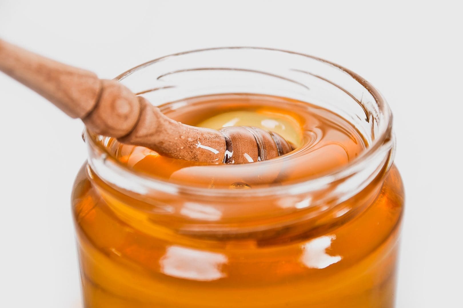 A detailed close-up of a wooden honey dipper in a jar filled with golden honey.